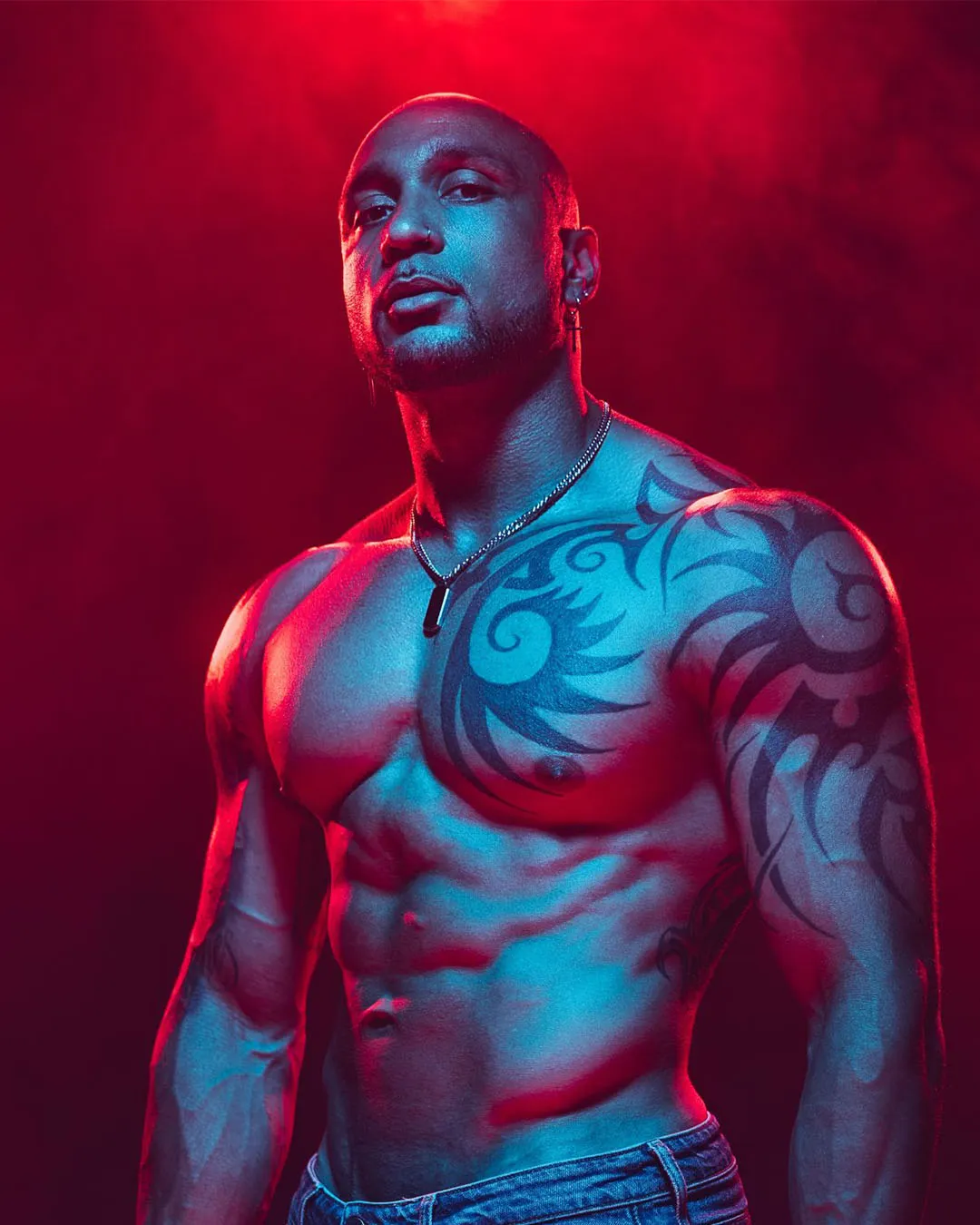 Nelly, artiste des Golden Boys, torse nu tatoué sur fond rouge