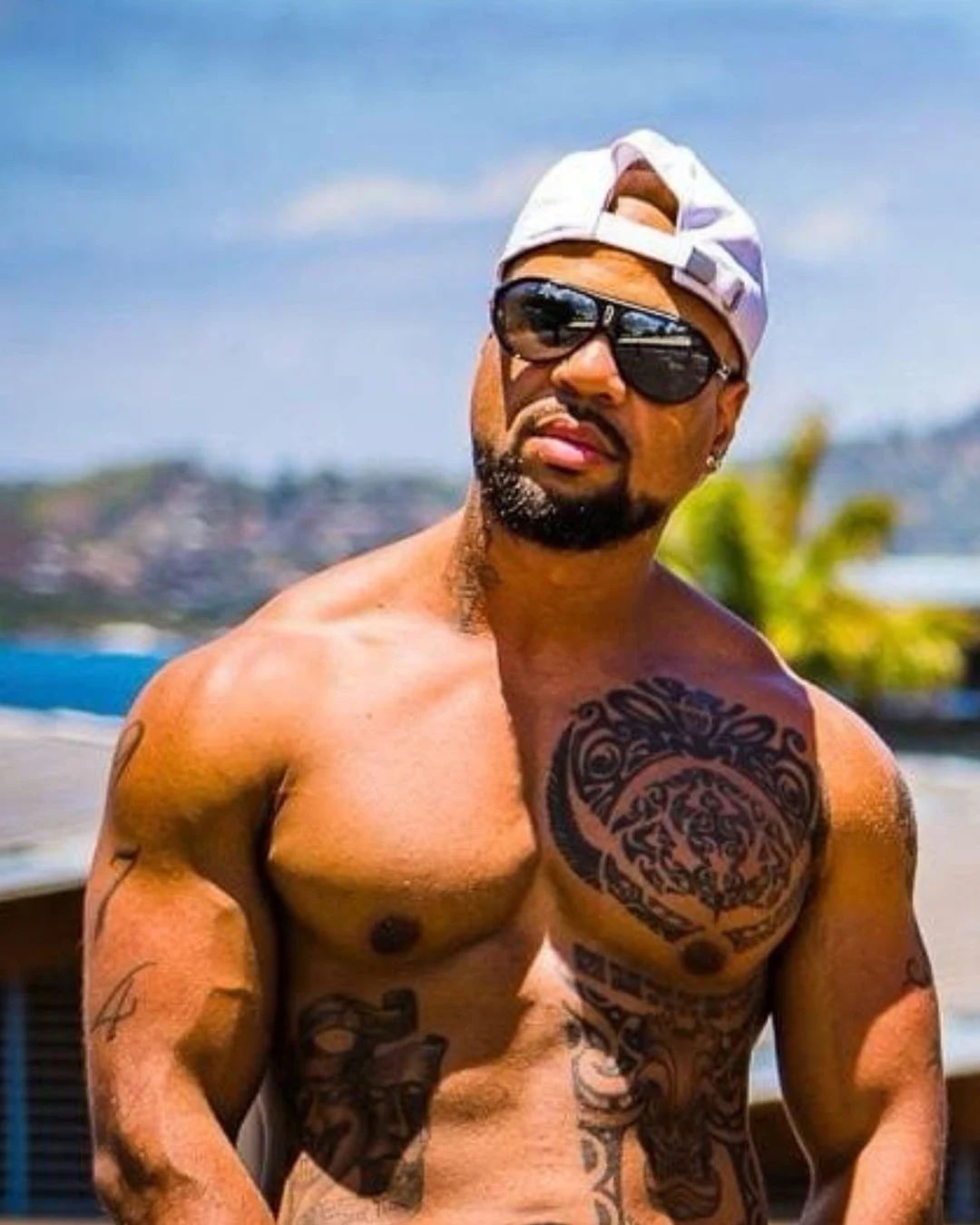 Ross, artiste des Golden Boys, posant torse nu en extérieur avec casquette